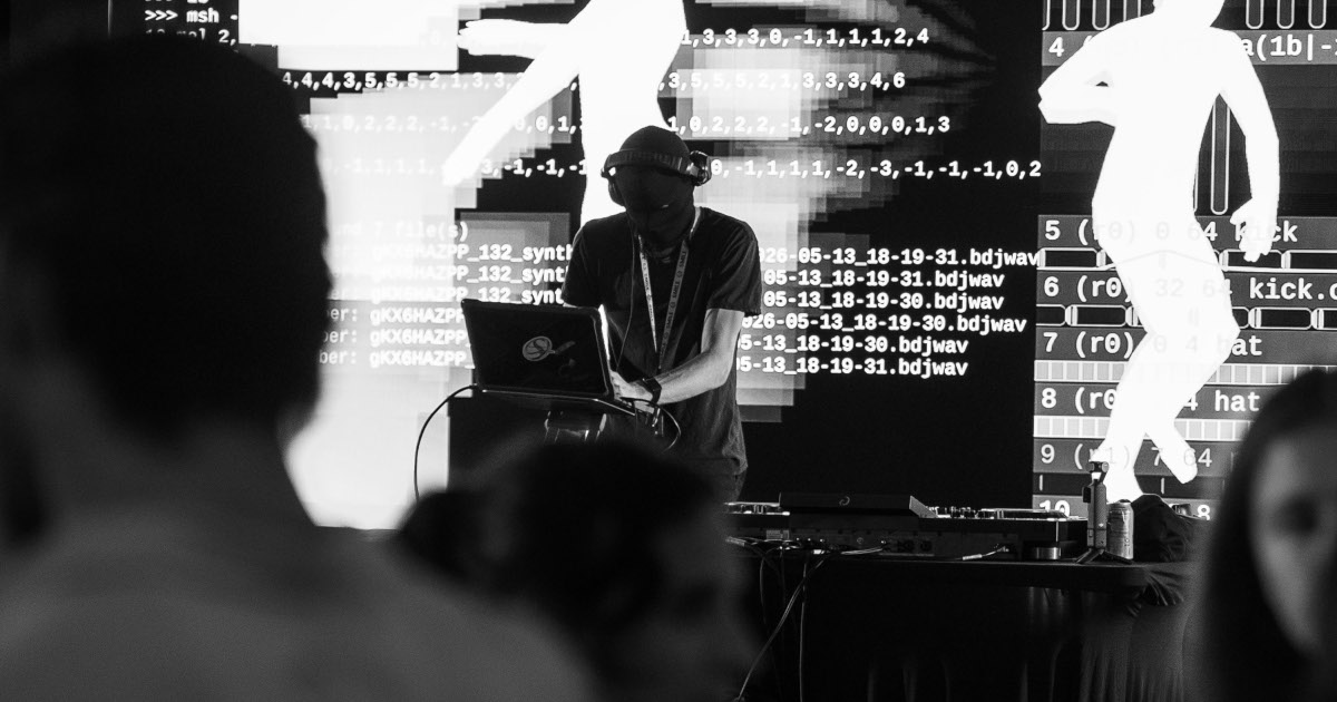 A live coder performing a techno set on Auwen, with the command line and visuals projected behind them